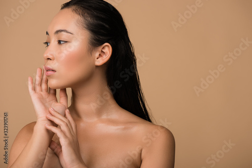 beautiful naked asian girl  looking away and touching face isolated on beige photo
