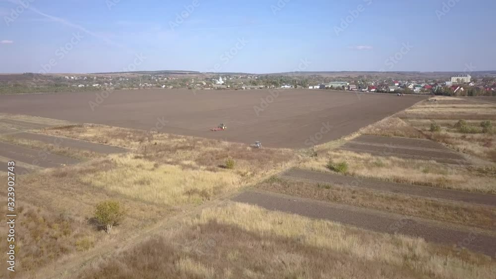 Top down aerial view of green tractor cultivating ground and seeding a dry field. Farmer preparing land with seedbed cultivator as part of pre seeding activities in early spring season. Top down aerial view of green tractor cultivating ground and seeding a dry field. Farmer preparing land with seedbed cultivator as part of pre seeding activities in early spring season.