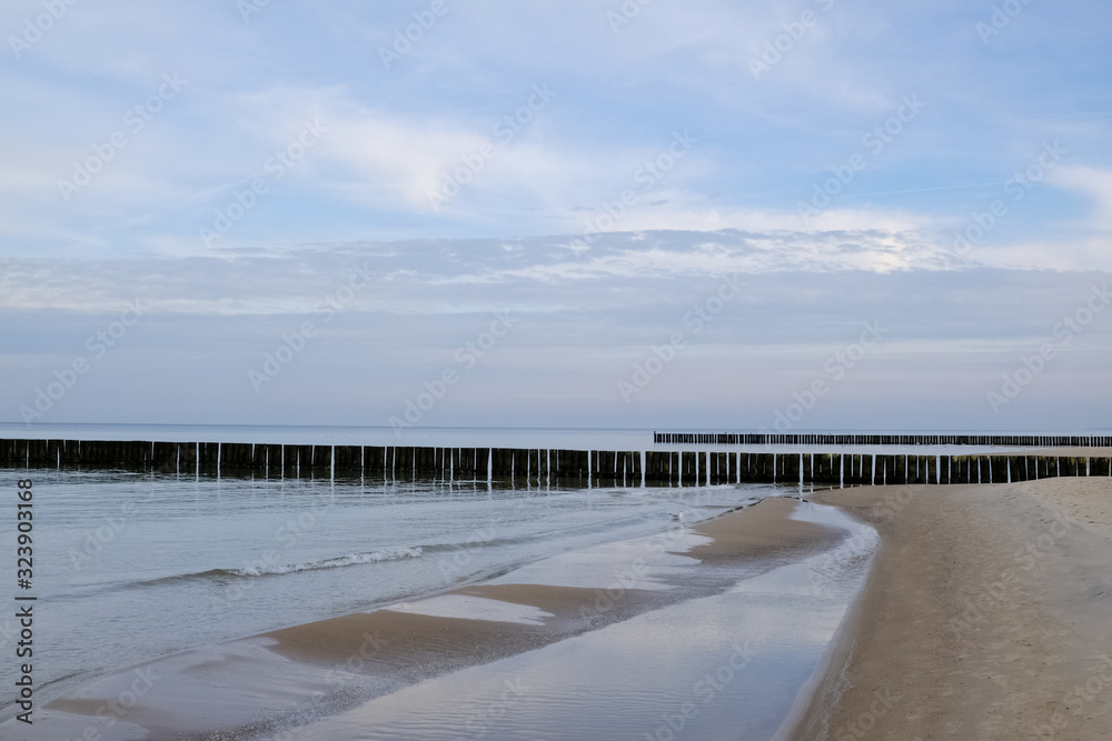 Breakwaters on the beach and beautiful blue sky with clouds in Dziwnowek / Poland on the Baltic Sea.