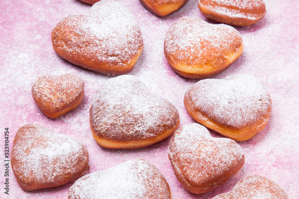 Homemade heart sheped donuts with powdered sugar on pnk background. Tasty doughnuts on cute pink pastel background