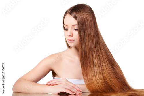 Woman with long brown hair sitting at table with his hands folded on it, looking at camera and isolated on white background