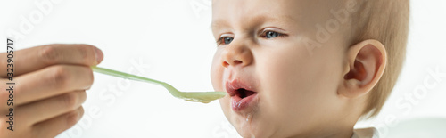 Selective focus of mother feeding baby on feeding chair isolated on white, panoramic shot