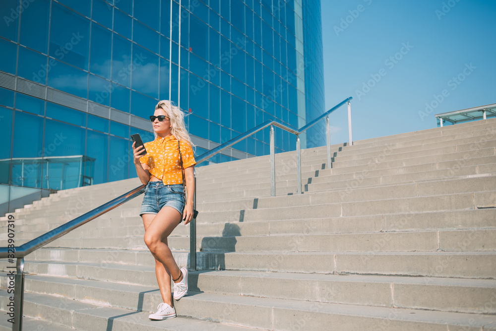 Trendy woman with smartphone standing on staircase