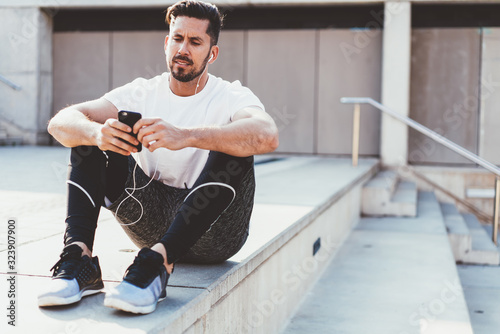 Handsome male athlete browsing smartphone with earphones at city street