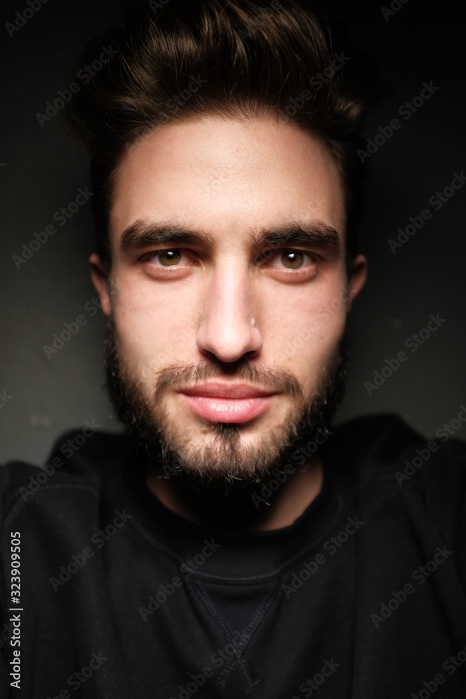 young handsome male with beard, mustache and trendy hairdo, wears casual grey sweater, has serious expression, poses in studio against gray background