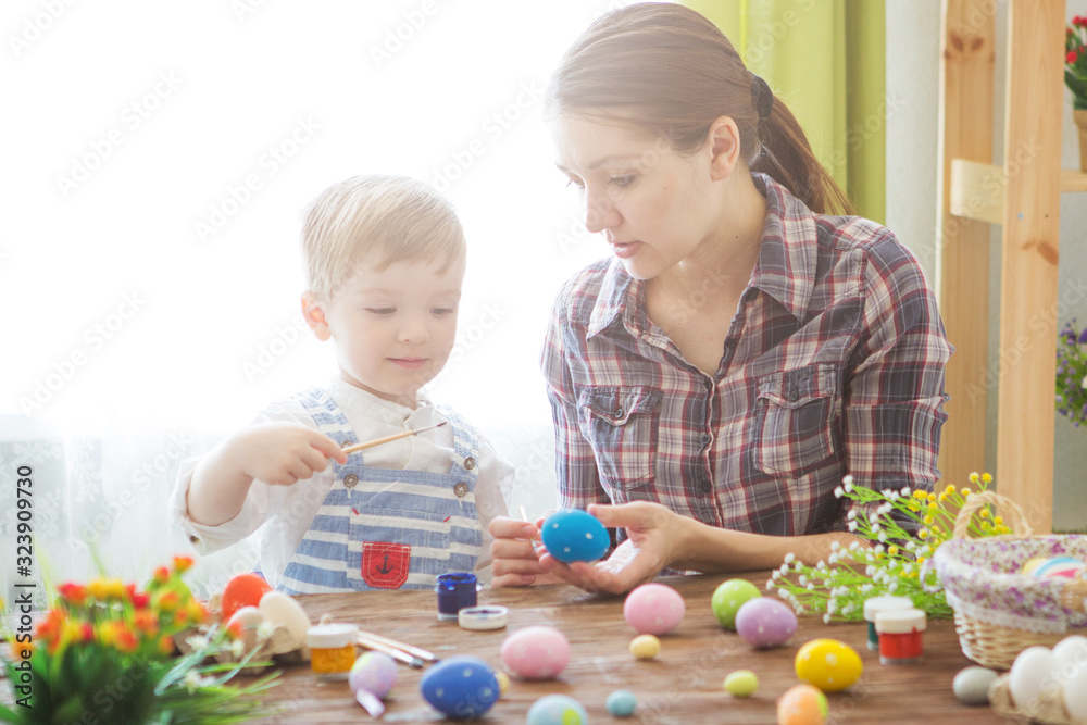 Naklejka premium Easter concept. Happy mother and her cute child getting ready for Easter by painting the eggs
