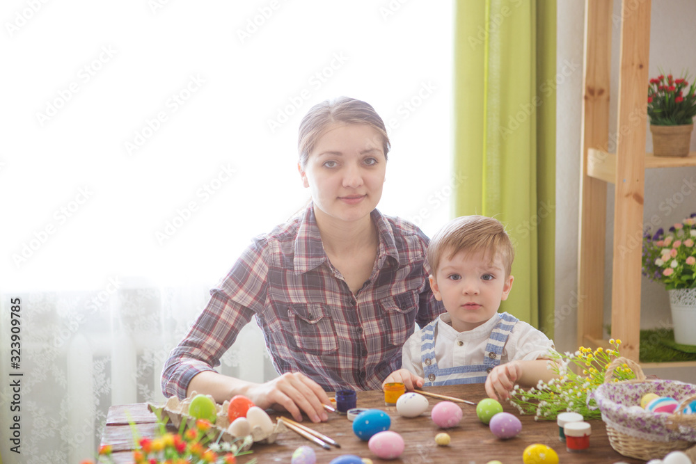 Obraz premium Mother and her son painting Easter eggs. Happy family preparing for Easter day