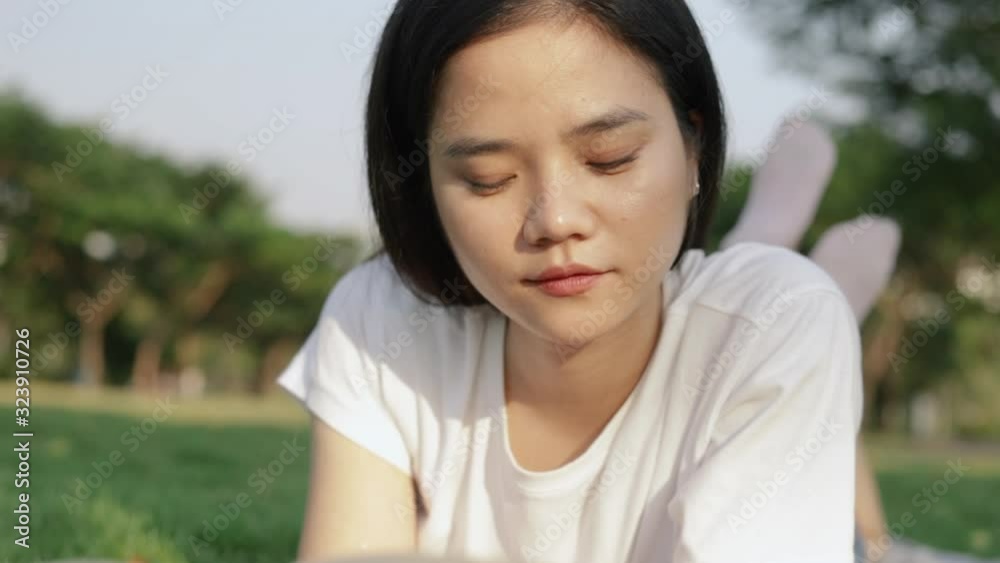 Attractive beautiful young asian female relaxed reading a book while lying on the floor grass outdoors at a public park on the beautiful sunset. Attractive beautiful young asian female relaxed reading a book while lying on the floor grass outdoors at a public park on the beautiful sunset.