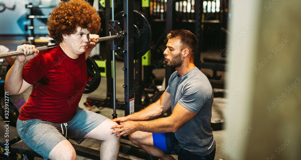 Overweight young man exercising gym with personal trainer