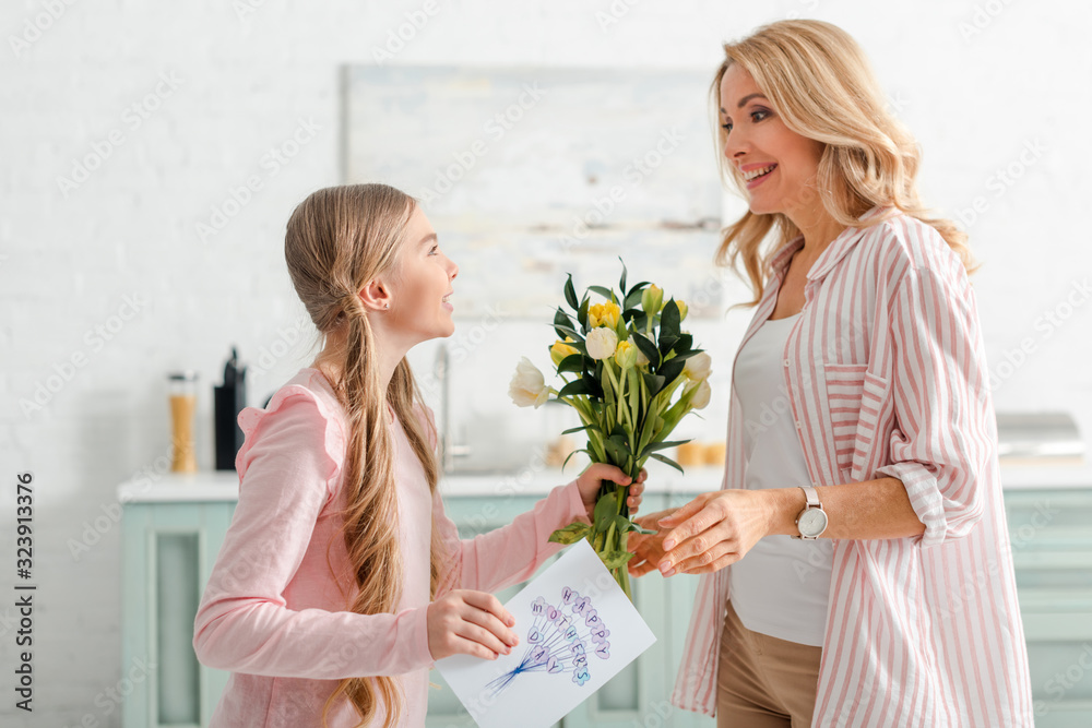 cheerful kid holding tulips and greeting card with happy mothers day lettering near mother cheerful kid holding tulips and greeting card with happy mothers day lettering near mother