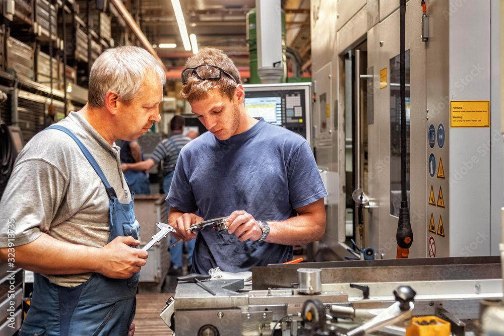 Skilled workers standing in a production hall in front of a machine tool, checking a workpiece Skilled workers standing in a production hall in front of a machine tool, checking a workpiece