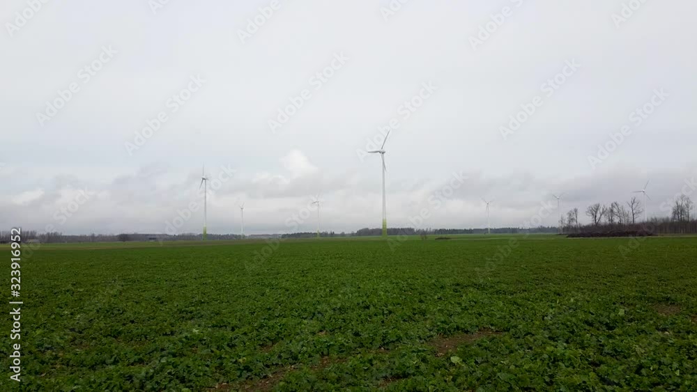 Aerial view of wind turbines generating renewable energy in wind farm, cloudy spring day, low flyover over green agricultural cereal fields, country side roads, wide angle drone shot moving forward Aerial view of wind turbines generating renewable energy in wind farm, cloudy spring day, low flyover over green agricultural cereal fields, country side roads, wide angle drone shot moving forward