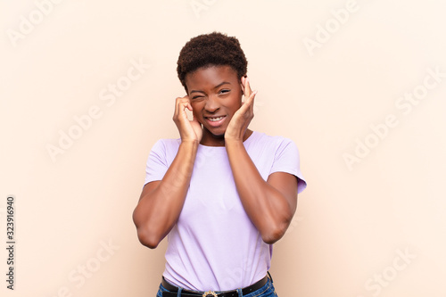 young pretty black womanlooking angry, stressed and annoyed, covering both ears to a deafening noise, sound or loud music photo