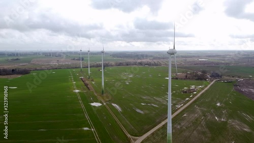 Aerial view of wind turbines generating renewable energy in wind farm in cloudy spring day, fresh green agricultural cereal fields, country side roads, wide angle drone shot moving forward photo