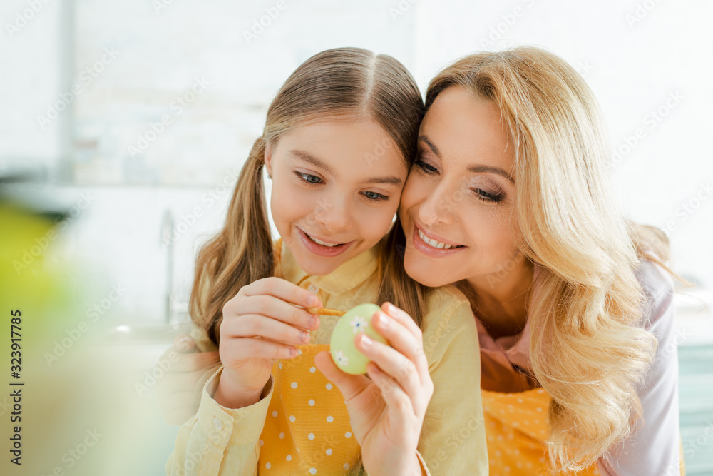 selective focus of happy mother near daughter painting easter egg selective focus of happy mother near daughter painting easter egg