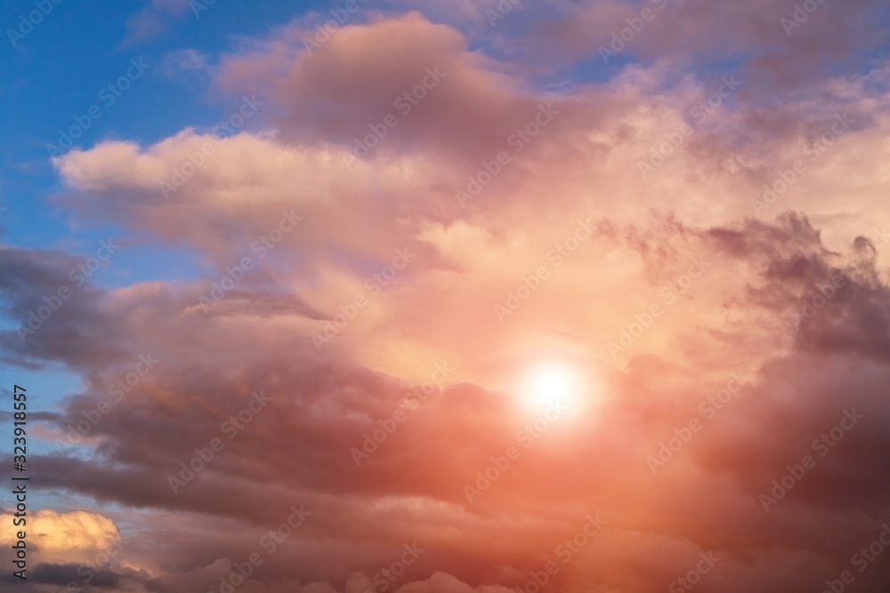 Fototapeta premium Dramatic sunset storm sky with cumulus clouds, orange sun and sunlight on blue sky background