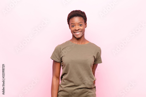 young pretty black womanlooking happy and goofy with a broad, fun, loony smile and eyes wide open against pink wall photo