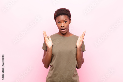 young pretty black womanlooking shocked and astonished, with jaw dropped in surprise when realizing something unbelievable against pink wall photo