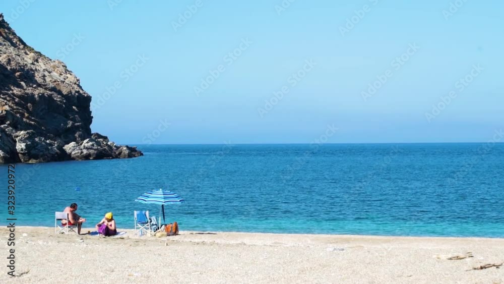 A man and woman enjoy a peaceful, tranquil, quiet, clear day at the Aeagean Sea on Zorgos beach, a hidden gem on the Greek island of Andros. A man and woman enjoy a peaceful, tranquil, quiet, clear day at the Aeagean Sea on Zorgos beach, a hidden gem on the Greek island of Andros.