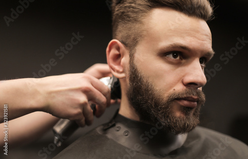 A confident look. Close-up shot of a young masculine man who is having his hair trimmed with an electric razor by a professional barber.