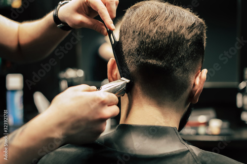 Trimming process. Close up photo of male hands grooming hair of his customer using a razor blade and comb.