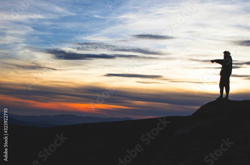 man on top of a mountain points the horizon towards a mountain landscape at sunset © javiemebravo