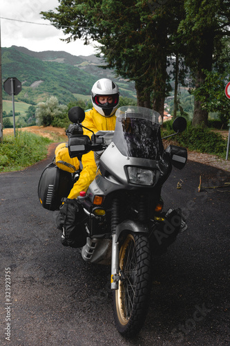 Motorcyclist traveler girl wearing yellow raincoat and sitting in a motorcycle saddle. Motorbike on mountain road. Extreme travel tour. Biker equipment. Vertical photo