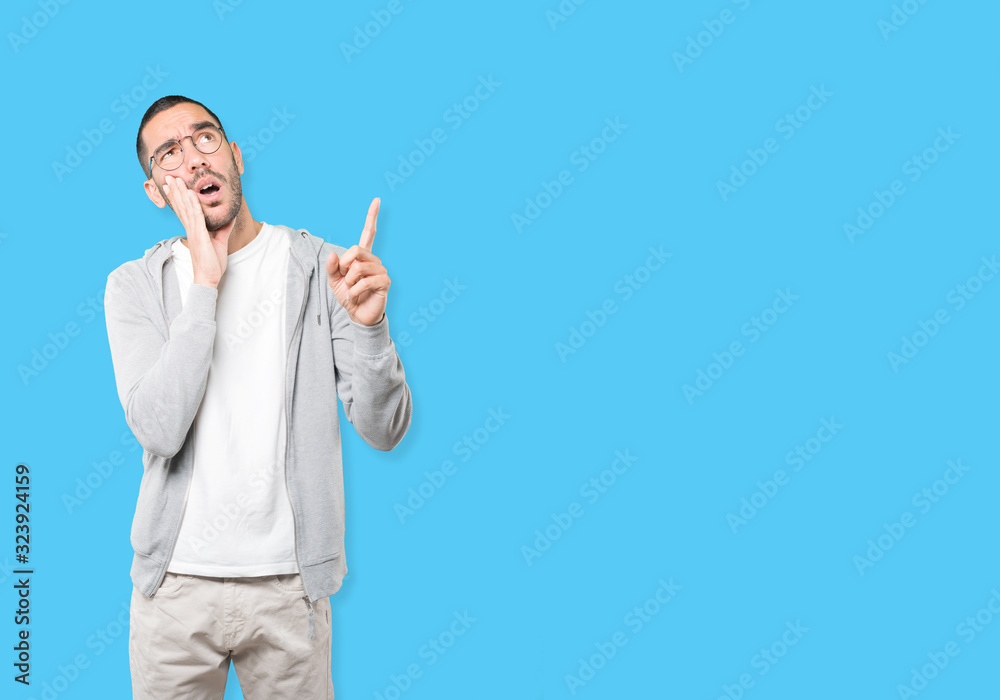 Hesitant young man pointing up with his finger Hesitant young man pointing up with his finger