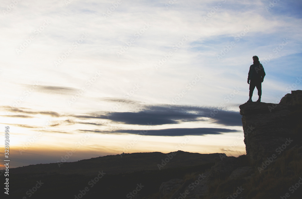 Liberty sensation. Man standing on the edge of a precipice facing a mountain landscape at sunset Liberty sensation. Man standing on the edge of a precipice facing a mountain landscape at sunset