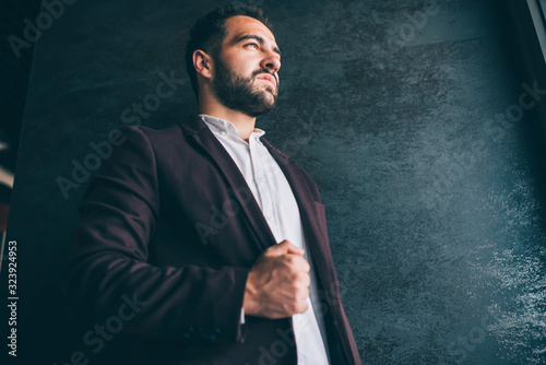 Serious caucasian prosperous male owner dressed in trendy expensive outfit looking away thoughtfully, handsome successful confident businessman posing near wall promotional background indoors. photo