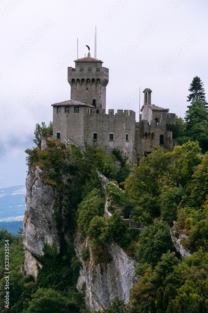 View from the top of the mountain to the medieval fortification. Dramatic mystical weather with fog. Castle in San Marino (Seconda Torre) Second Tower, Vertical photo