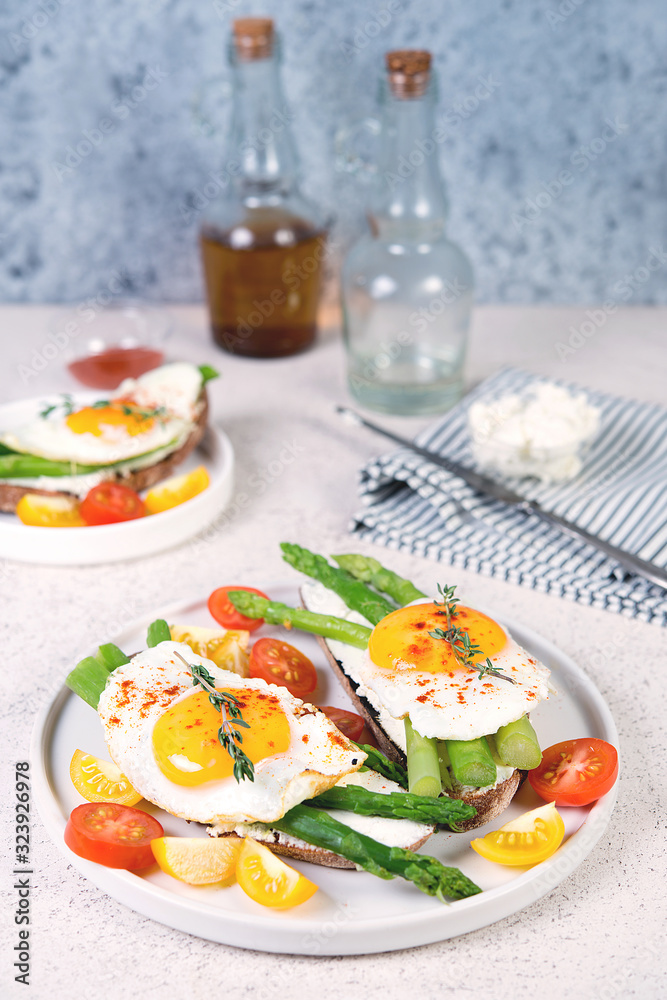 Two toasts with asparagus, ricotta and fried egg on black bread. Vertical photo, selective focus.