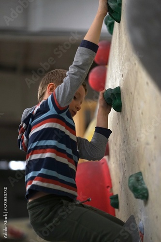 Little boy with blonde hair and striped shirt is climbing  bouldering in an indoor boulder hall          