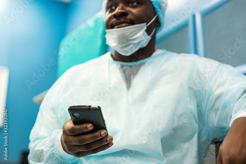 Portrait of a surgeon in uniform and medical mask after the operation is completed sitting with a phone in his hands