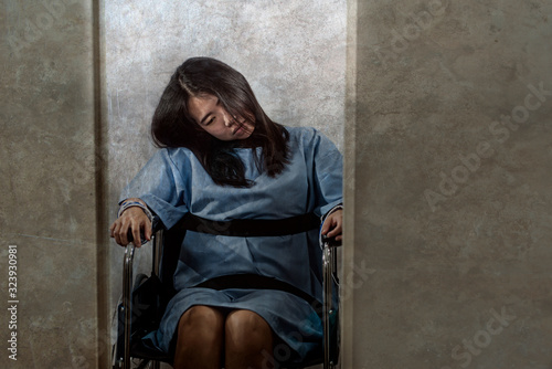 young crazy and mentally insane Asian woman restrained in wheelchair at mental hospital suffering psychiatric disorder as schizophrenia looking catatonic