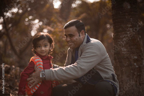 An Indian brunette father and his baby boy in winter garments enjoying themselves in winter afternoon on a  dry grass field in green natural  background. Indian lifestyle and parenthood.