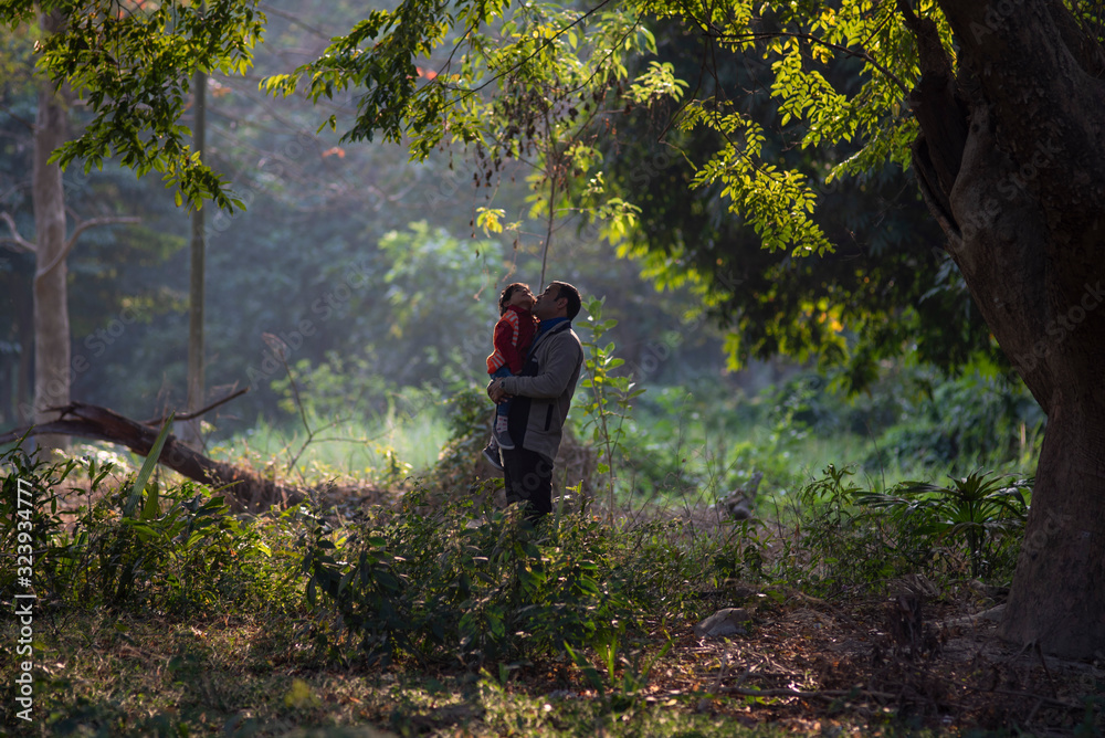 An Indian Telugu brunette father and his baby boy in winter garments enjoying themselves in winter afternoon on a green grass field in forest background. Indian lifestyle and back light photography. An Indian Telugu brunette father and his baby boy in winter garments enjoying themselves in winter afternoon on a green grass field in forest background. Indian lifestyle and back light photography.