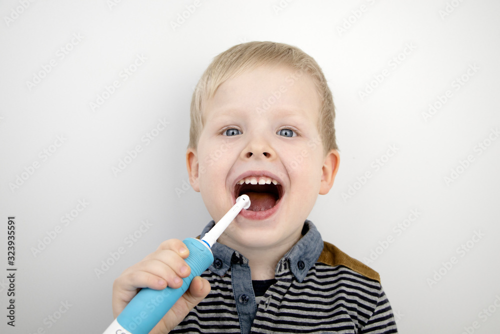 Four year old child brushes his teeth with an electric brush. The boy on a white background laughs and holds a toothbrush. The concept of baby teeth and oral hygiene Four year old child brushes his teeth with an electric brush. The boy on a white background laughs and holds a toothbrush. The concept of baby teeth and oral hygiene