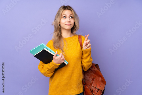 Teenager Russian student girl isolated on purple background with fingers crossing and wishing the best