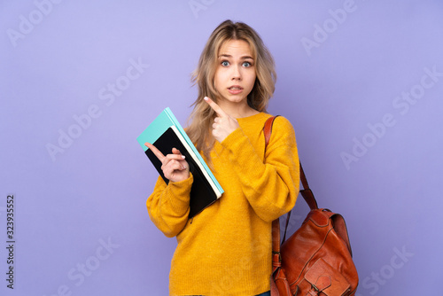 Teenager Russian student girl isolated on purple background frightened and pointing to the side