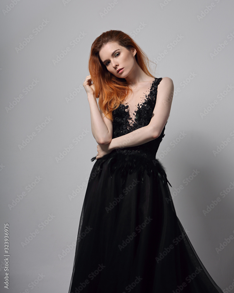 Beautiful elegant young model with bright foxy hairstyle posing in fashion chic black dress with long skirt on studio Beautiful elegant young model with bright foxy hairstyle posing in fashion chic black dress with long skirt on studio