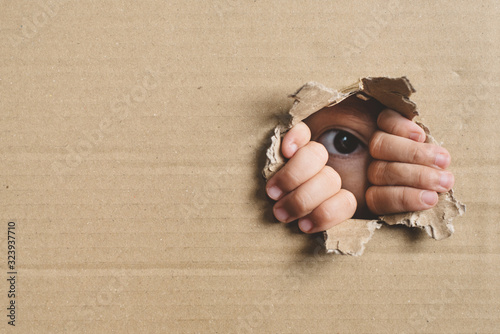 Little girl peeking from a hole on cardboard box. Concept of a human trafficking, Spying and Curiosity