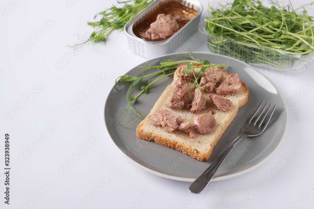 Healthy food, Sandwich with cod liver and peas microgrines on a plate on a white background