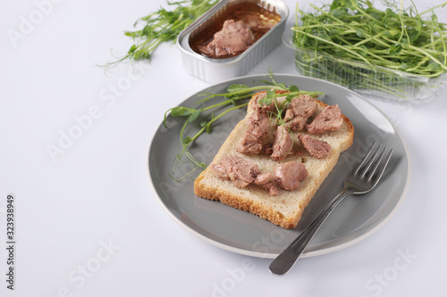 Healthy food, Sandwich with cod liver and peas microgrines on a plate on a white background