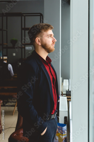 Portrait of a young successful businessman in a suit in the office. Close-up standing by the window
