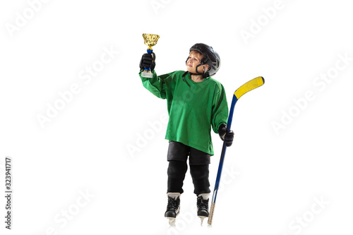 Champion. Little hockey player with the stick on ice court and white studio background. Sportsboy wearing equipment and helmet training. Concept of sport, healthy lifestyle, motion, movement, action.