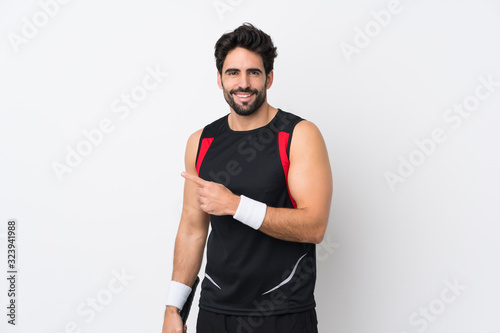 Young handsome man with beard over isolated white background playing tennis and pointing to the lateral