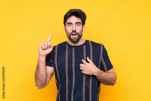 Young handsome man with beard over isolated yellow background with surprise facial expression