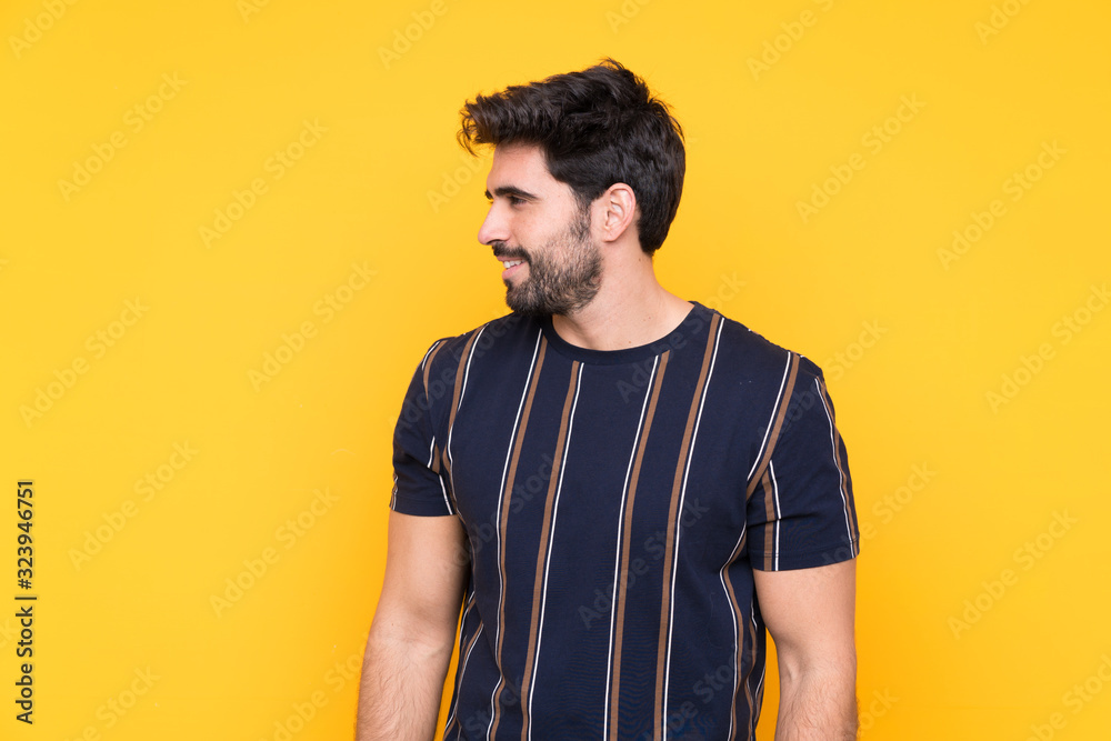 Young handsome man with beard over isolated yellow background looking to the side