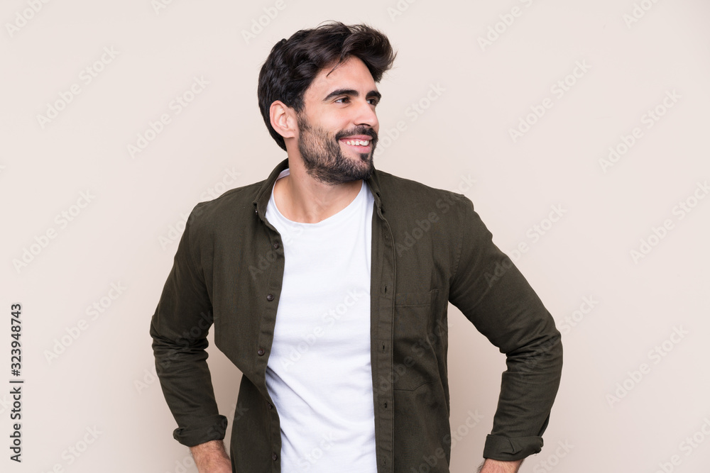 Young handsome man with beard over isolated background posing with arms at hip and smiling Young handsome man with beard over isolated background posing with arms at hip and smiling